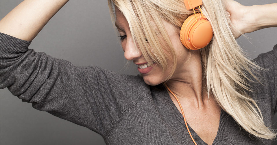 Woman with blonde hair listening to earphones and smiling.